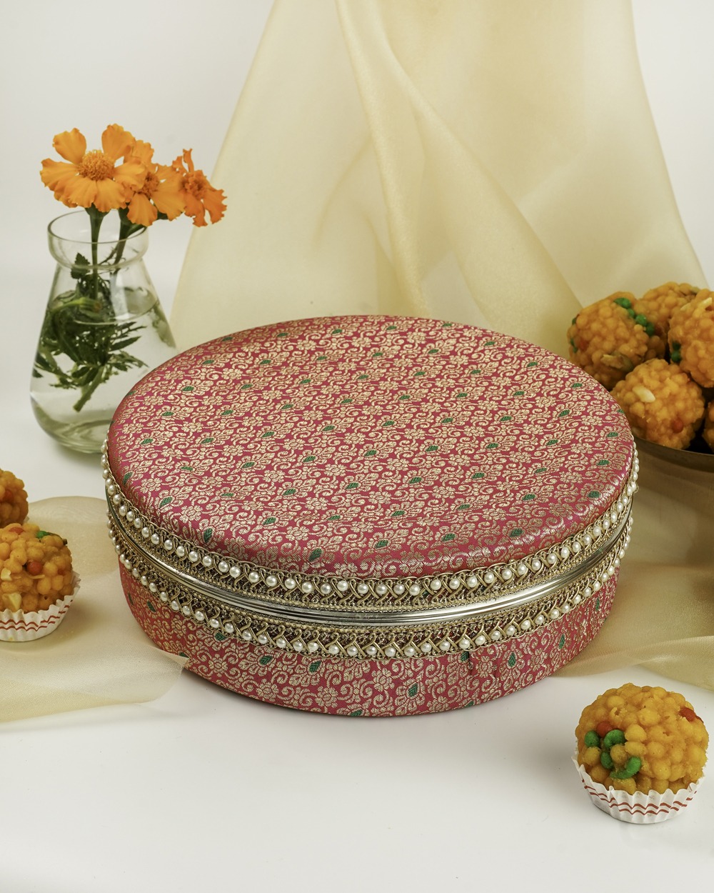Vibrant pink Gulzar Ladoo Box by Navka Studio with gold and green brocade, silver lace, and pearl trim, displayed with sweets.