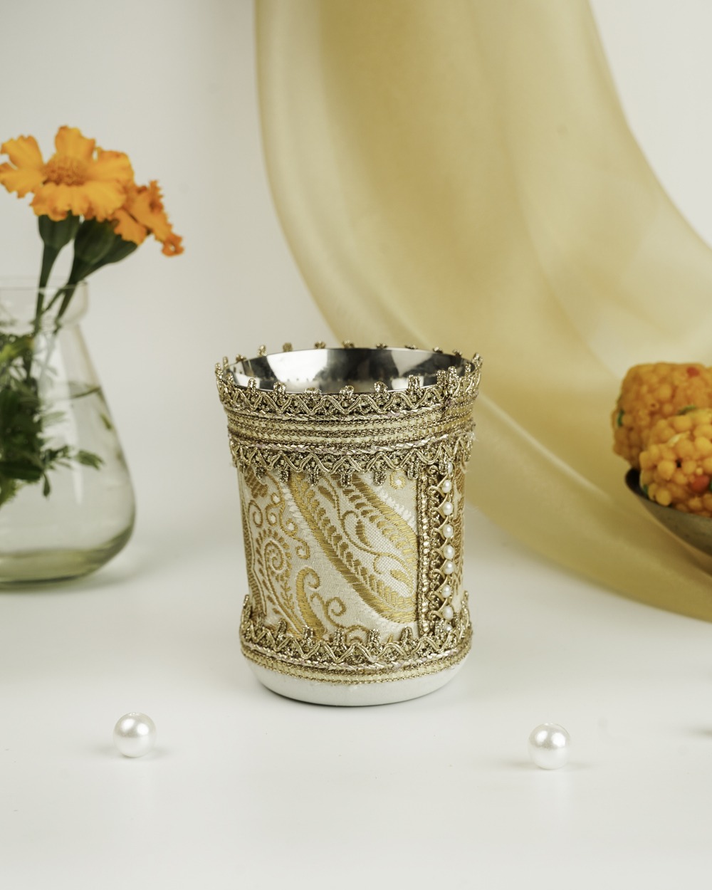 An elegant Noori Brocade Glass by Navka Studio, wrapped in cream and gold brocade fabric with intricate lace and pearls.