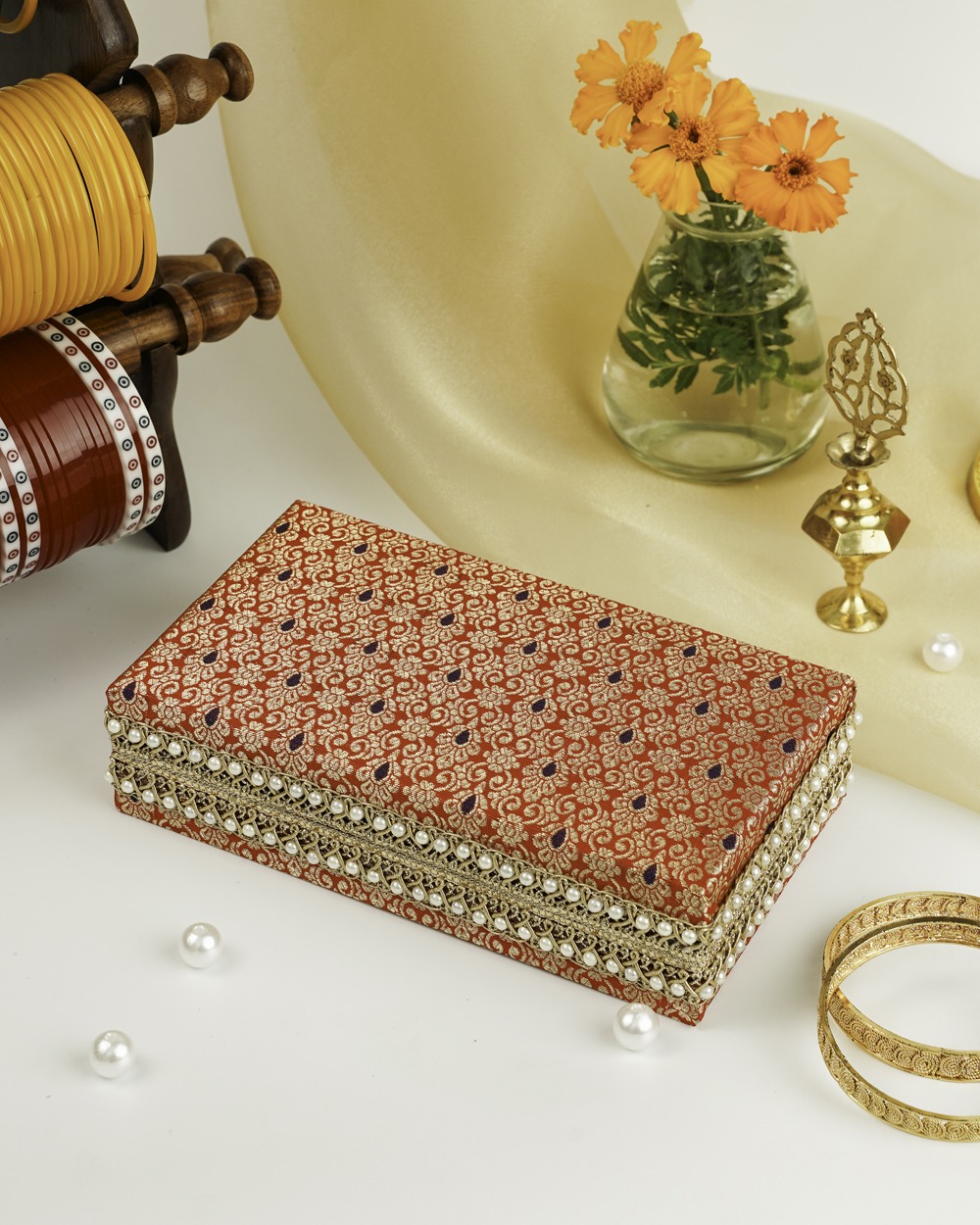 A rectangular Sindoori Double kada box by Navka Studio, in red brocade with gold/purple patterns, gold lace, and pearl trim.