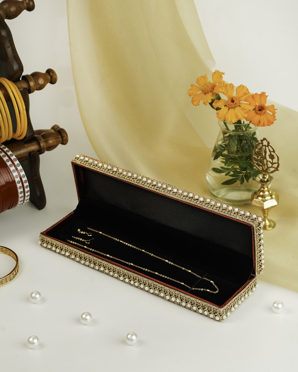 A red Sindoori Brocade Chain Box by Navka Studio, open to show a gold chain on black lining, with pearl and lace trim.