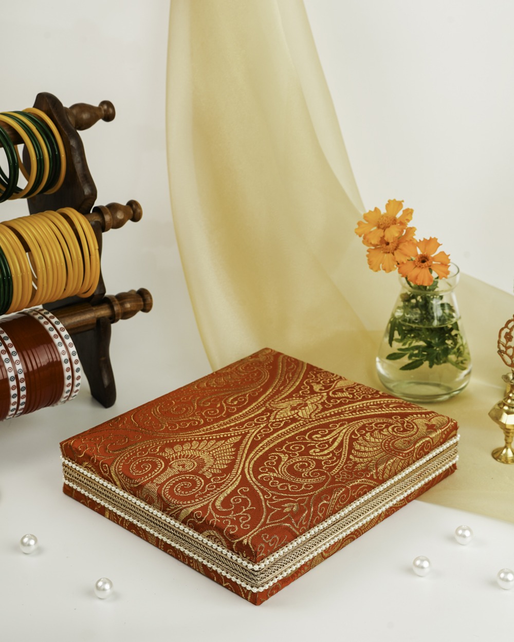 The elegant Sindoori Paisley Brocade Necklace Box by Navka Studio, shown closed to highlight its beautiful red and gold paisley fabric and delicate pearl border.