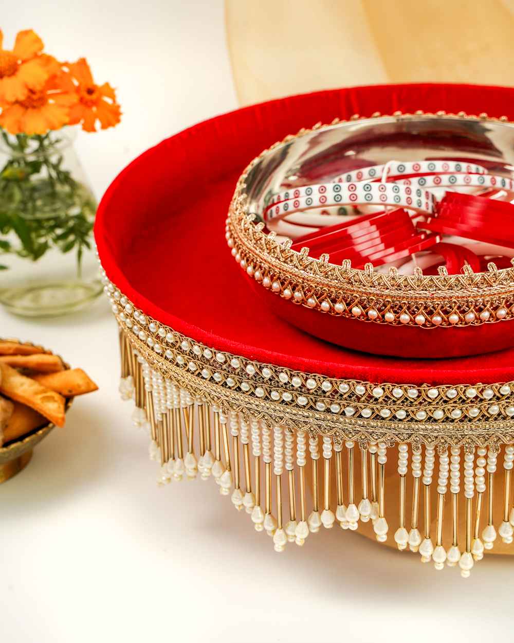 A Sindoori Velvet Chura Bowl by Navka Studio, on its matching red velvet tray with an elegant pearl and gold fringe, set on a festive table.