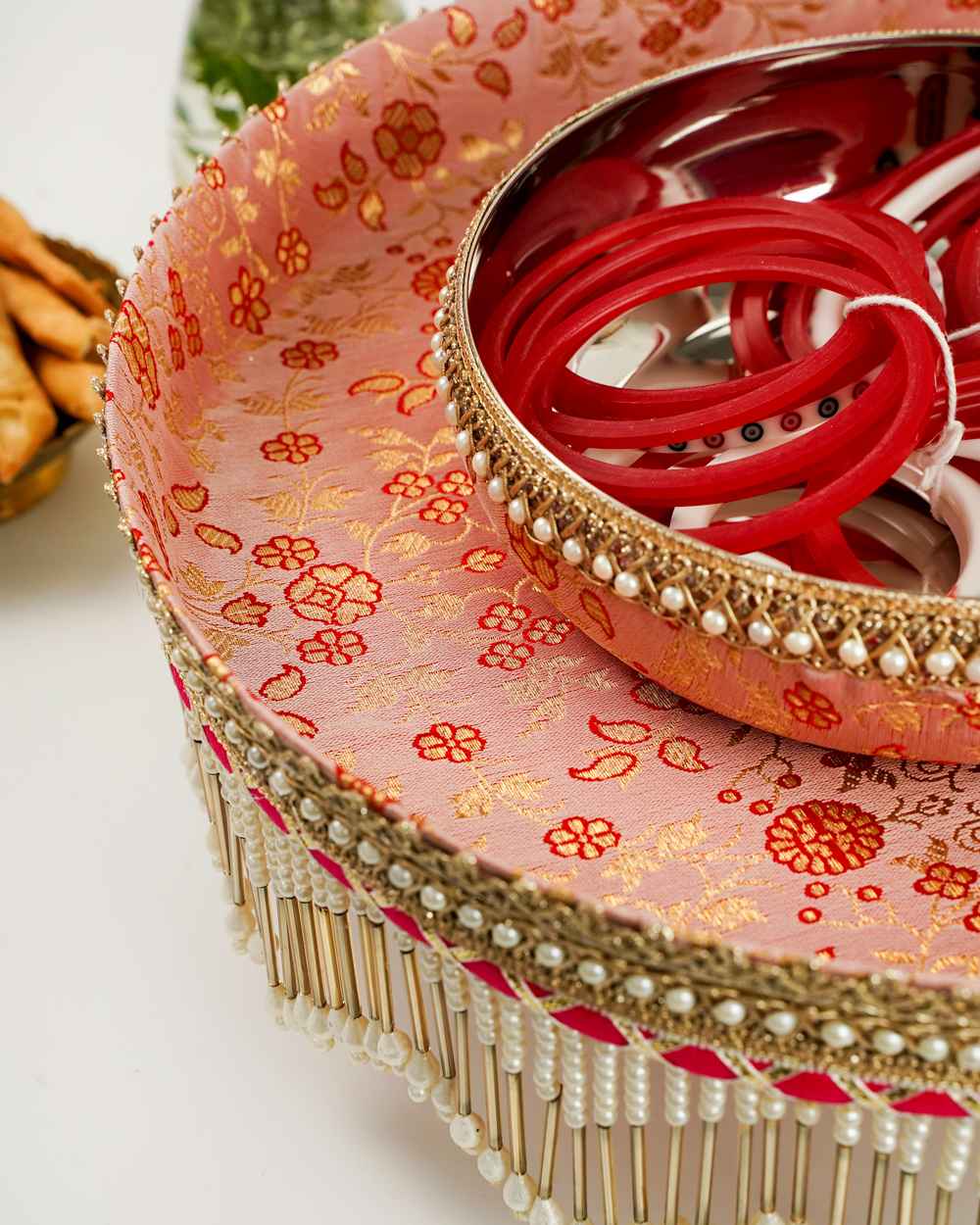 A close-up of the Bahaar Chura Bowl by Navka Studio, highlighting its pink floral brocade, pearl trim, and the tray's elegant pearl fringe.