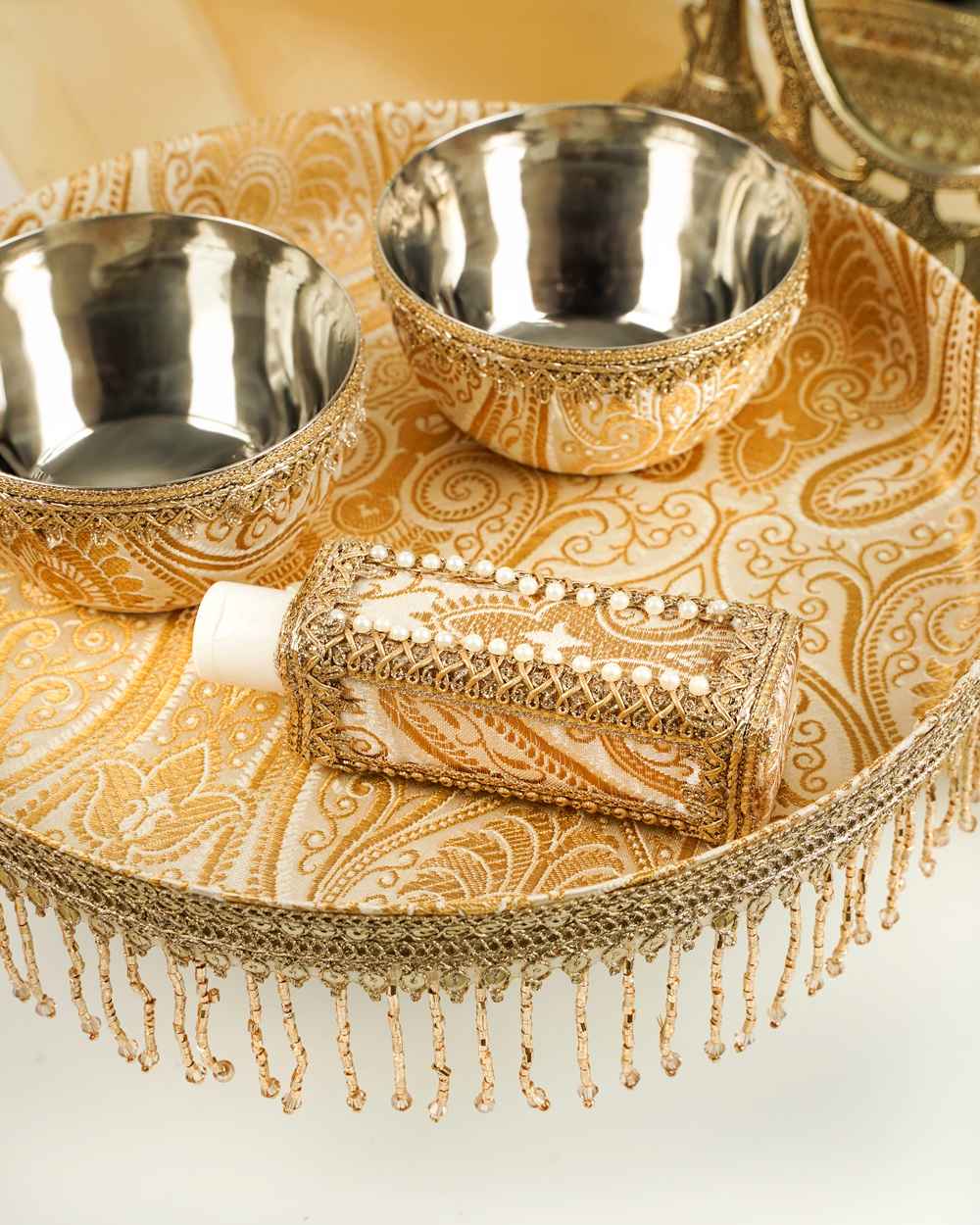 A Noori Haldi Thaal Set by Navka Studio in cream and gold brocade, with matching bowls, bottle, and a beaded gold fringe.