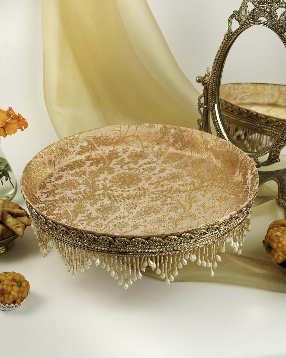 The stunning Meher Shagun Thaal with Cover by Navka Studio, shown empty to display its pink and gold brocade base, set on a festive table with a mirror and