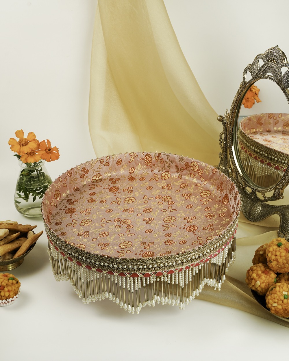 A close-up of the Bahaar Shagun Thaal with Cover by Navka Studio, showing its sheer net cover with gold motifs placed over ladoos, highlighting the thaal's intricate pearl and gold fringe.
