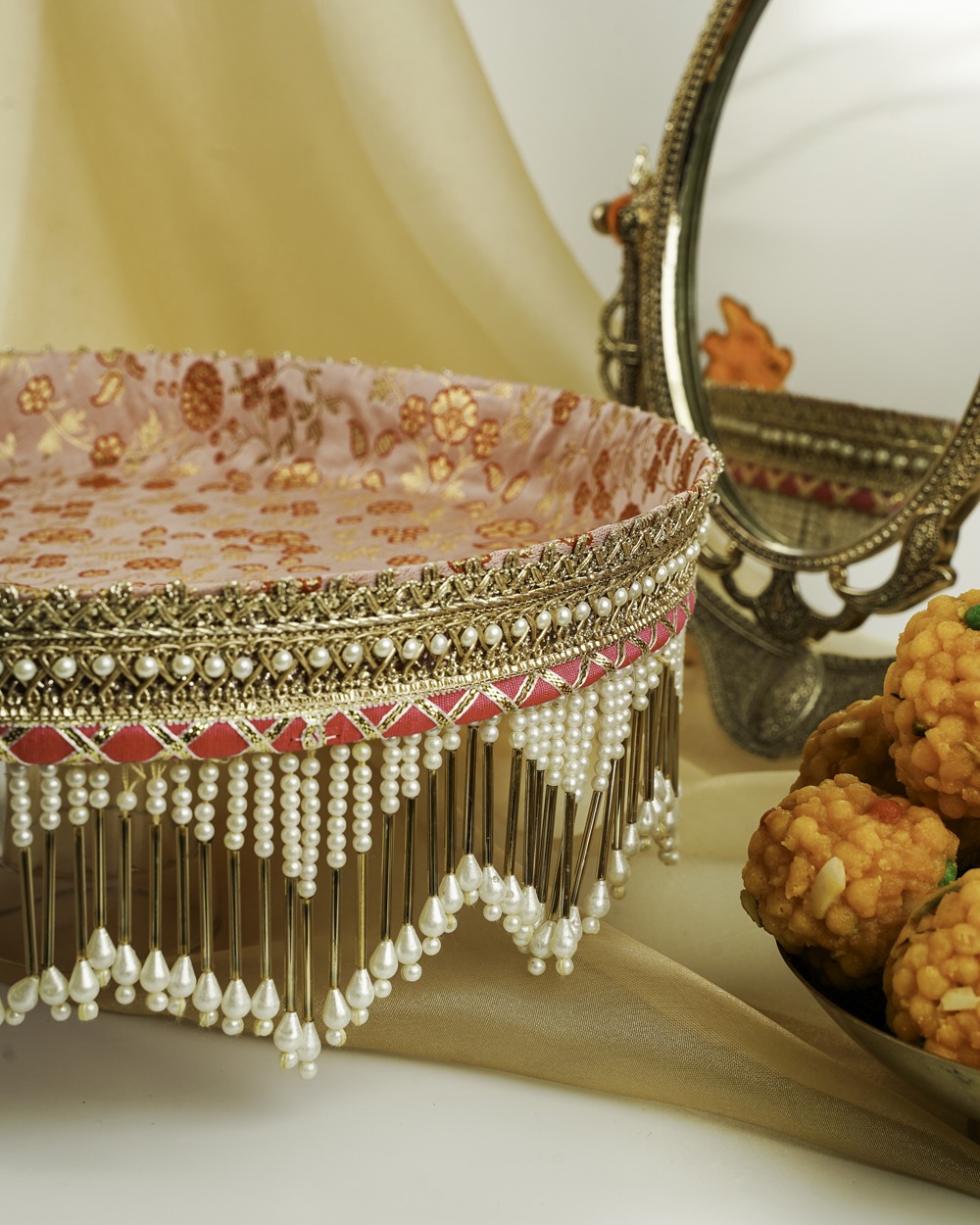 Bahaar Shagun Thaal with Cover | Navka Studio A detailed close-up of the Bahaar Shagun Thaal with Cover by Navka Studio, focusing on the thaal's stunning pearl and gold bar fringe, pink brocade base, and gold lace border.