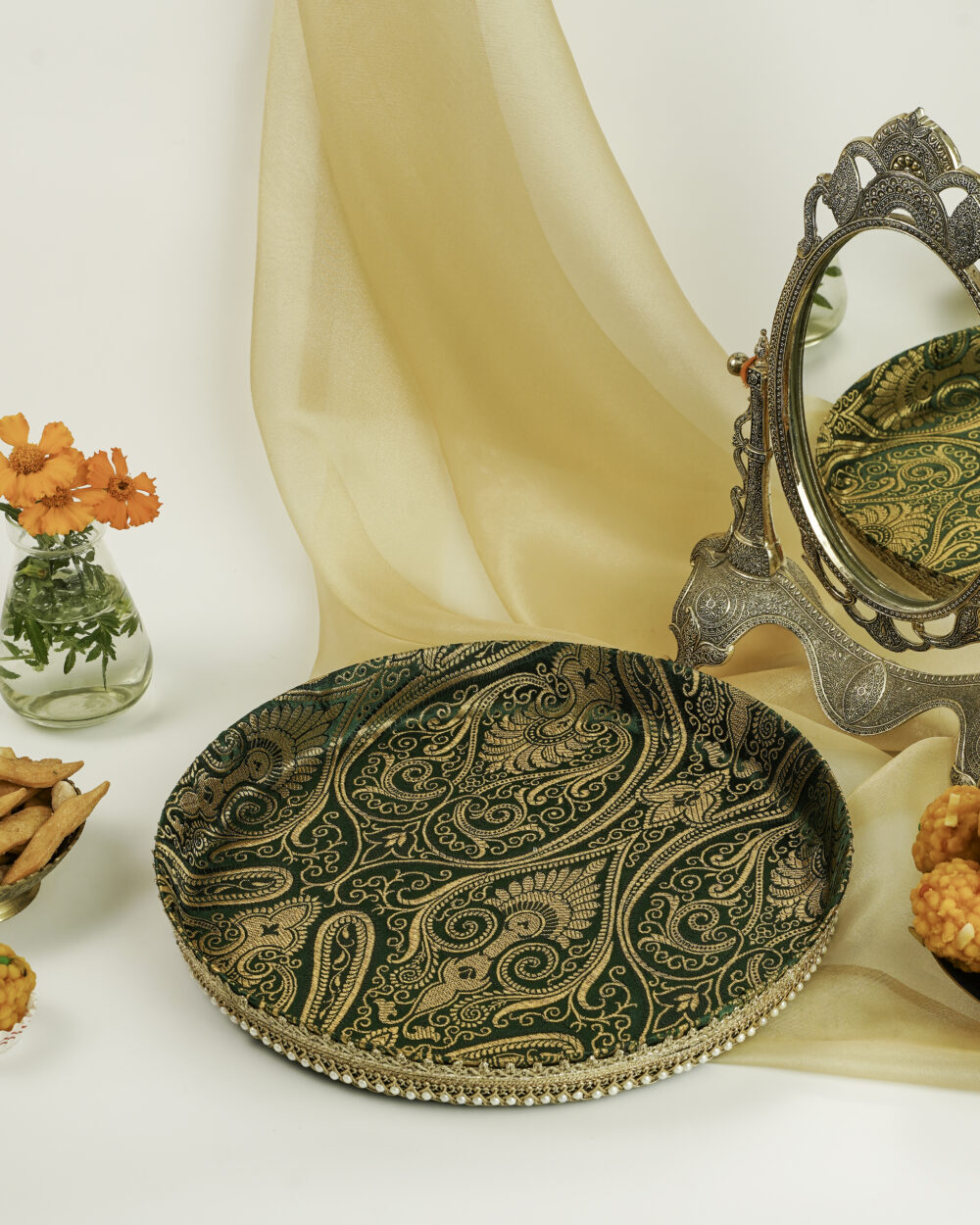 A green Baagh Shagun Thaal with Cover by Navka Studio, with gold paisley brocade and pearl trim, on a festive table.