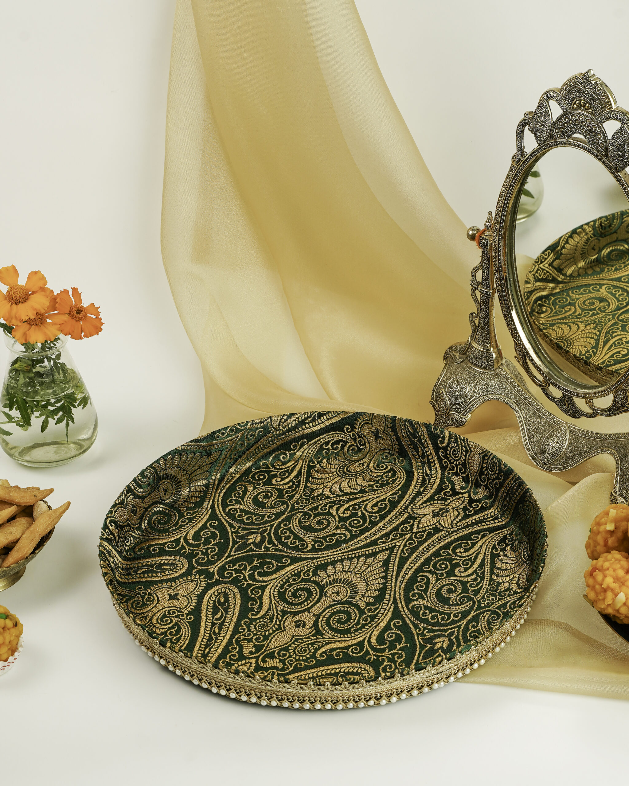 A green Baagh Shagun Thaal with Cover by Navka Studio, with gold paisley brocade and pearl trim, on a festive table.