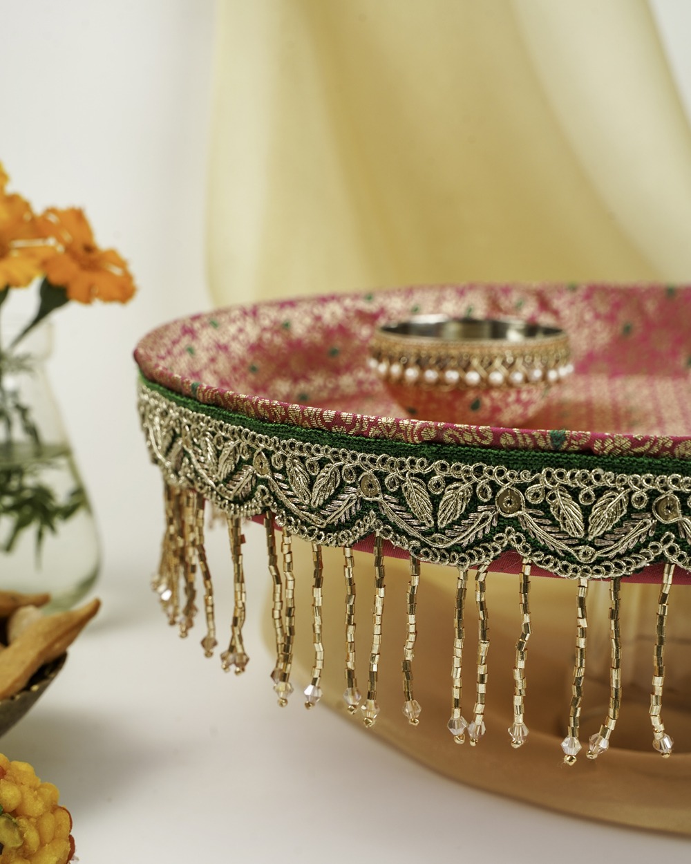 Sindoori Shagun Thaal with Cover for Shagun Ceremony Sindoori Shagun Thaal with Cover by Navka Studio – a close-up of an intricately designed pink and gold thaal with green lace, pearl hangings, and elegant bead detailing, perfect for festive rituals.