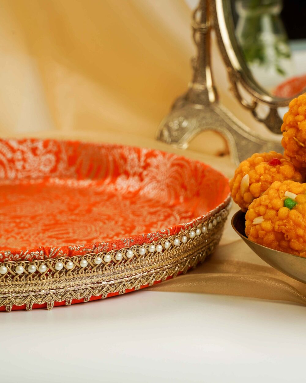 A close-up of the Sunehri Shagun Thaal with Cover by Navka Studio, detailing its orange brocade tray with gold lace and pearl trim.