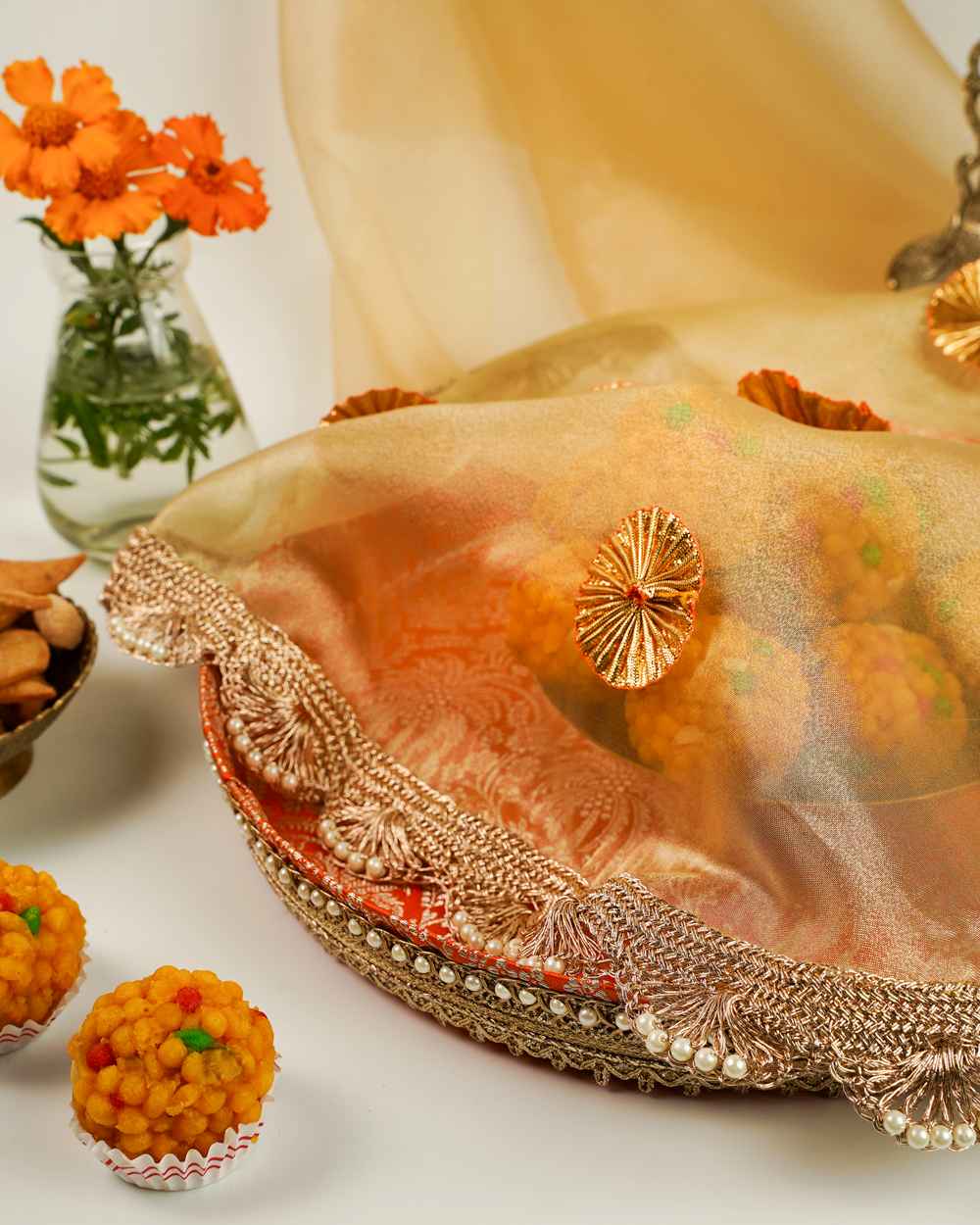 A Sunehri Shagun Thaal with Cover by Navka Studio, with a sheer gold cover, gota flowers, and pearl trim, over an orange brocade tray.