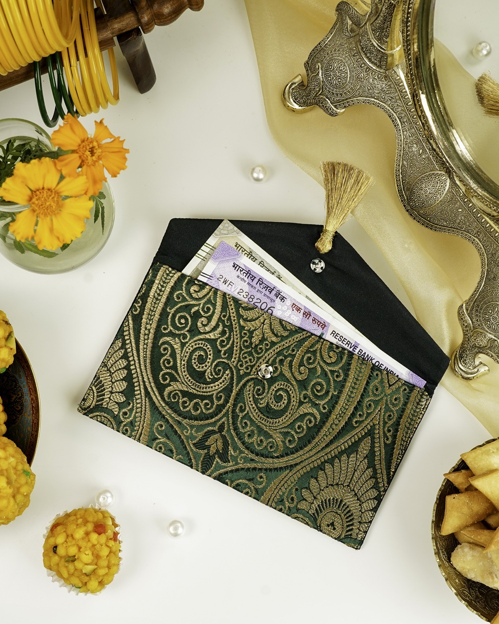 A green Baagh Brocade Shagun Envelope by Navka Studio, with gold paisley brocade, open to show currency notes inside.