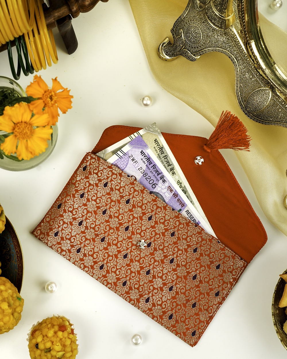 A red Sindoori Brocade Shagun Envelope by Navka Studio, with gold/purple brocade, open to show currency notes inside.