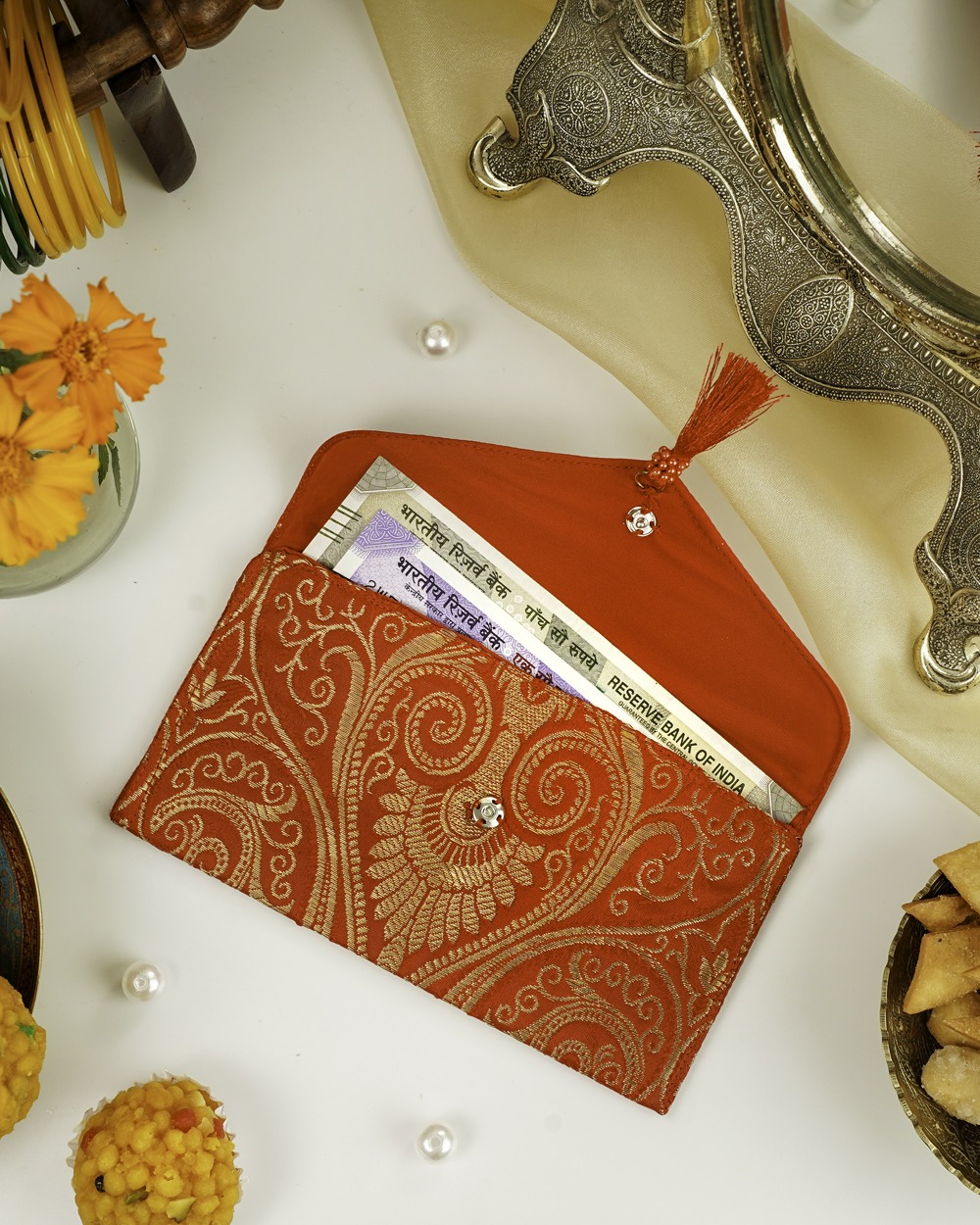 A red Sindoori Paisley Brocade Shagun Envelope by Navka Studio, with gold paisley brocade, open to show currency notes inside.
