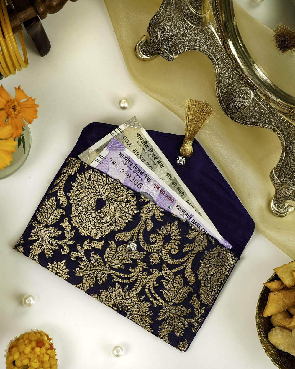 A navy blue Chandni Brocade Shagun Envelope by Navka Studio, with gold floral brocade, open to show currency notes inside.