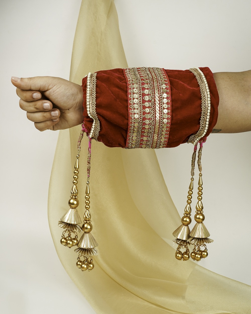 A red Gulzar Velvet Chura Cover by Navka Studio on an arm, with rich gold sequin lace and hanging gold jhumki tassels.