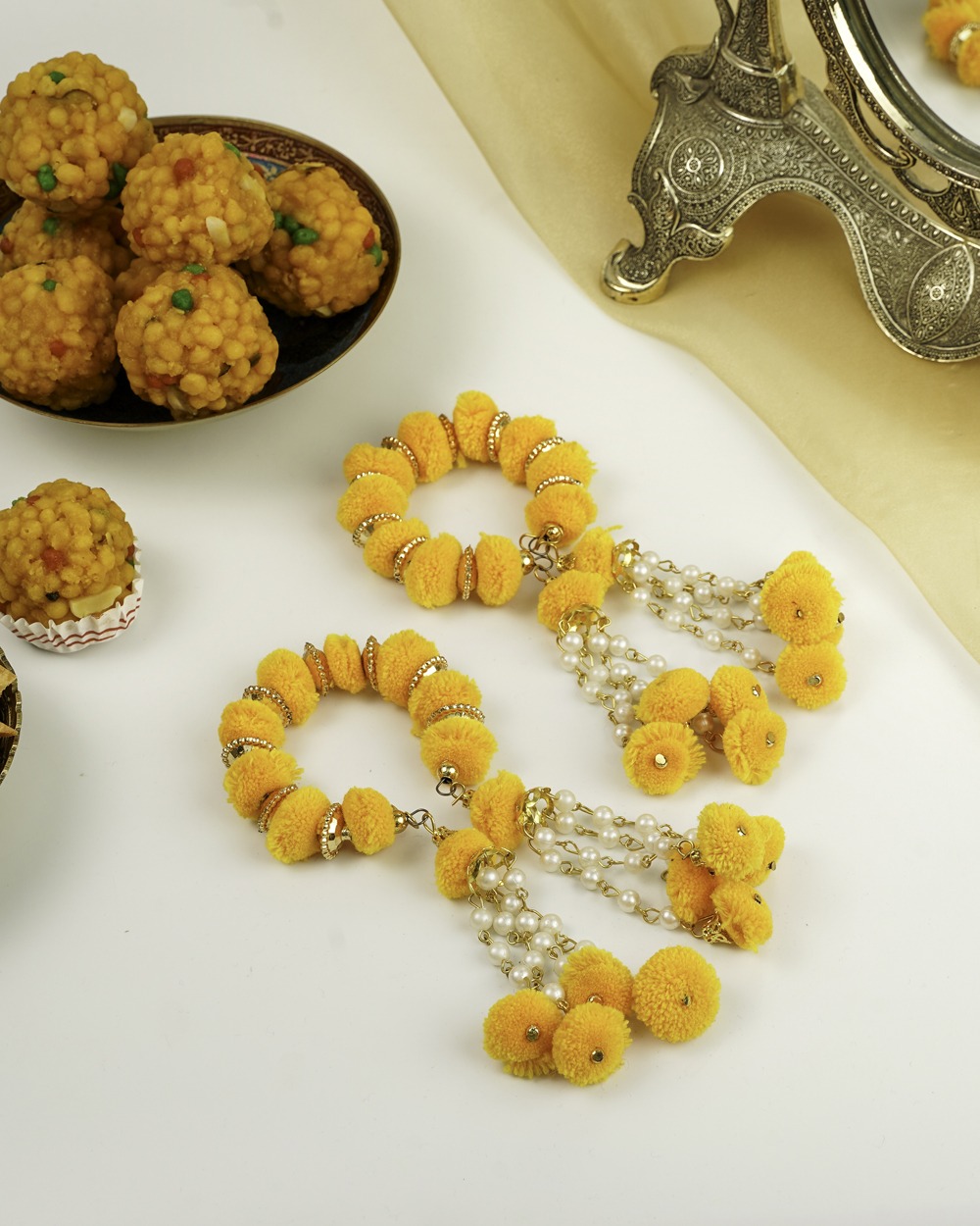 Two bright yellow Basant Gaane by Navka Studio, adorned with golden details and pearl tassels, beside ladoo sweets.
