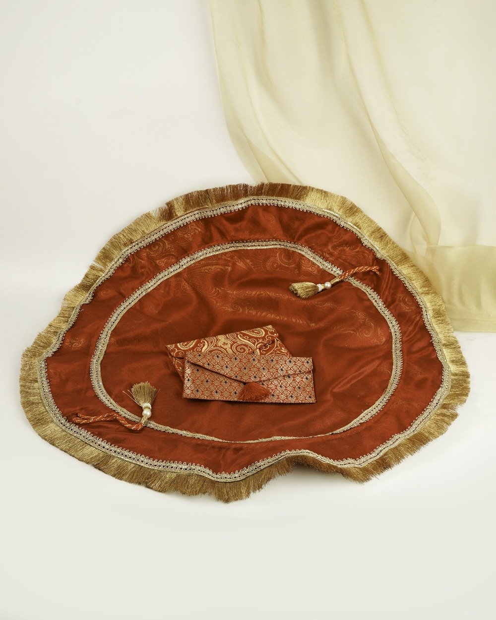A luxurious Sindoori Lap Cover by Navka Studio, in a rich red silk with golden paisley motifs, adorned with a wide gold fringe border, and styled with matching red and gold shagun envelopes.