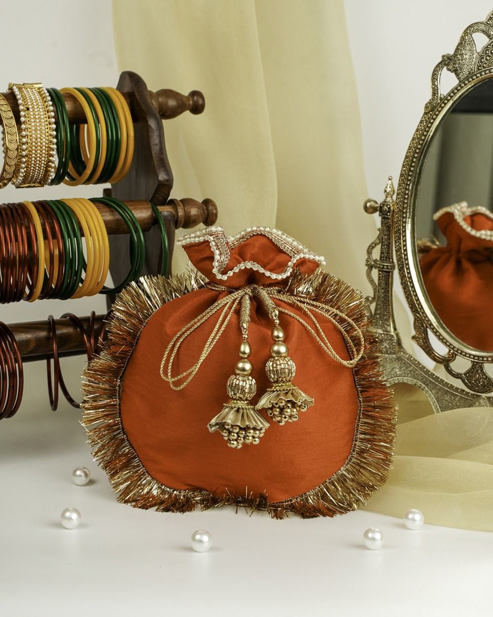 Navka Studio's striking Sunehri Silk Potli, crafted from rich orange silk with a wide, shimmery gold fringe trim, a red and gold brocade-style drawstring opening, and intricate gold beaded tassels.