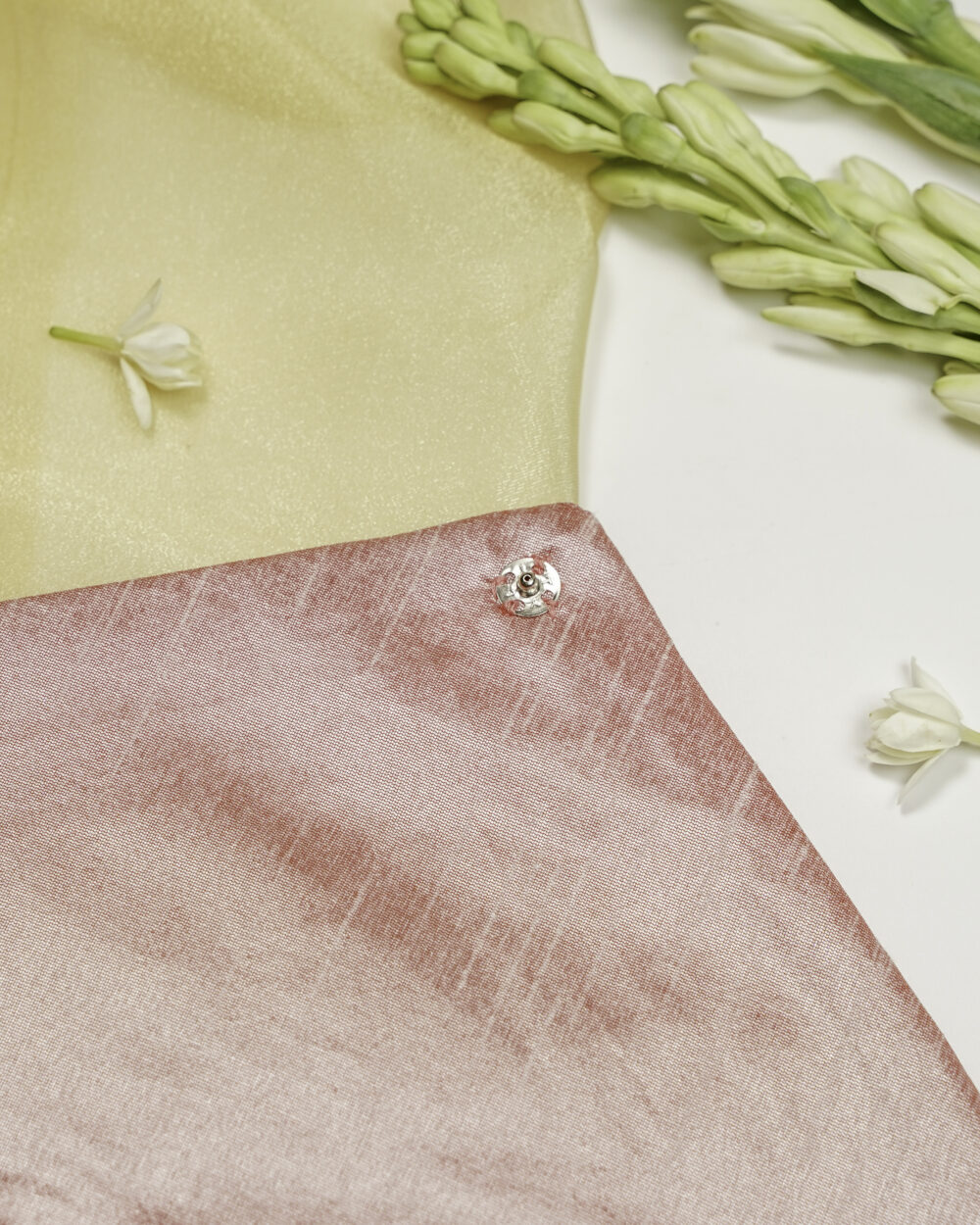 Close-up of Navka Studio Bahaar Silk, Grid Gota Work, Trousseau Bag showing the shiny silver floral button on the pink silk fabric, styled with golden drape and tuberose flowers.
